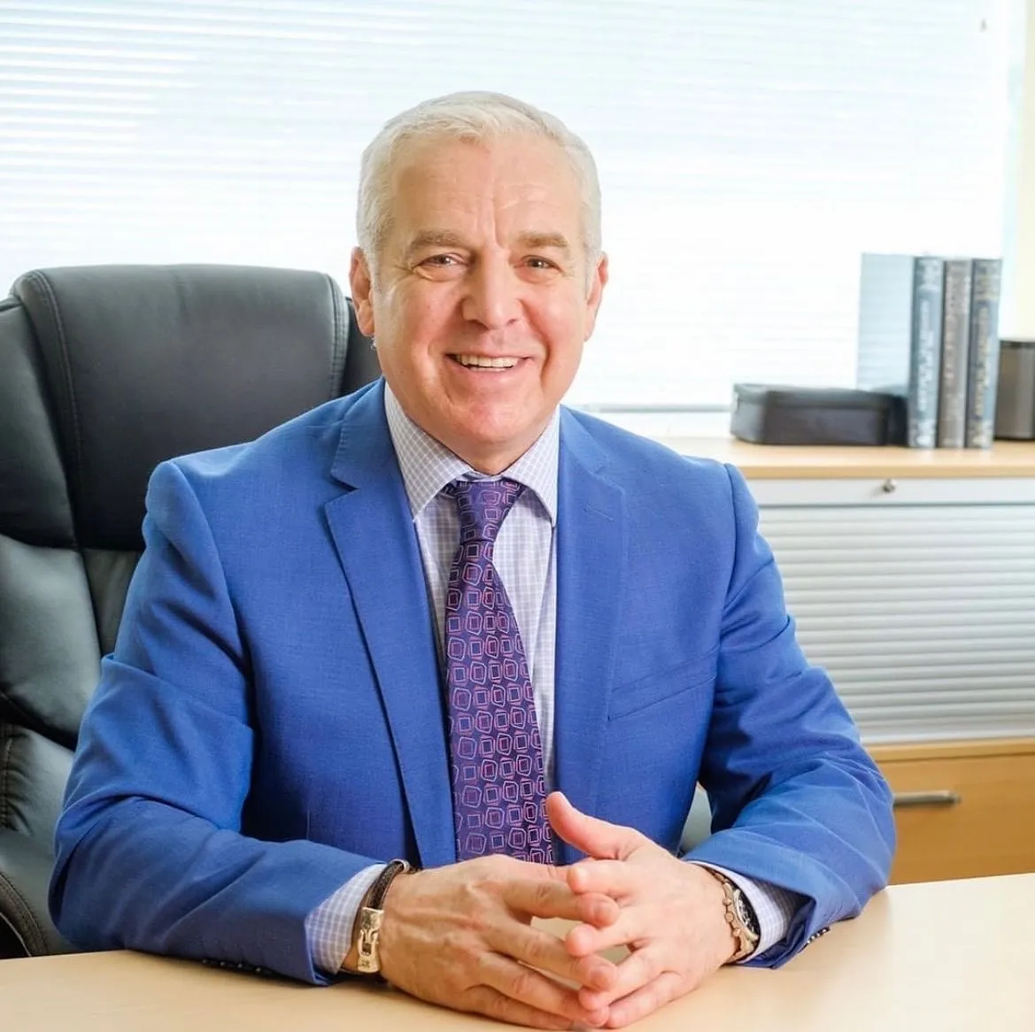 Dr. Boris Mordkovich sitting at his desk in his office, wearing a blue blazer and purple tie